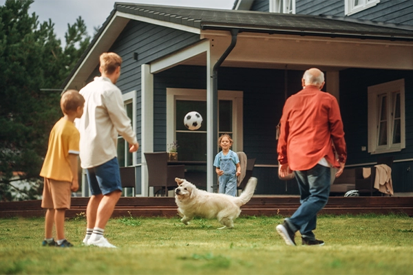 A close up of grass blades with a man riding a lawn mower and a house in the distance.