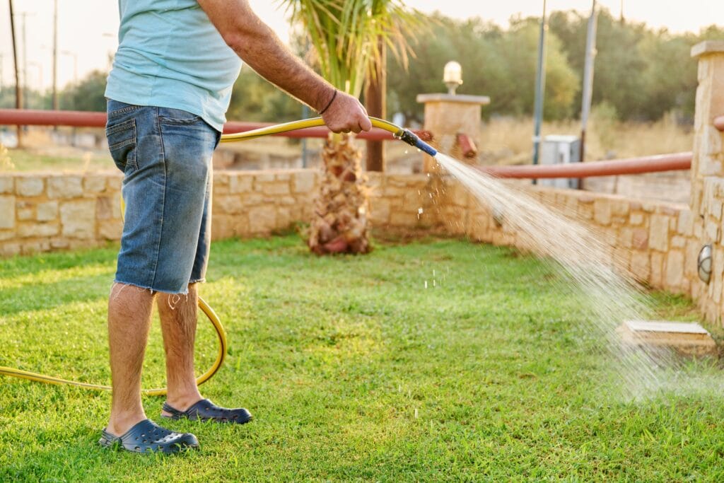 Homeowner watering grass with a hose as part of Florida lawn care tips for proper irrigation.