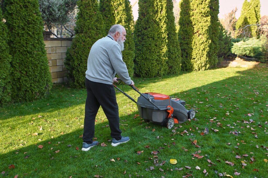 Elderly man preparing for seasonal lawn care, cleaning leaves from the yard and mowing the grass