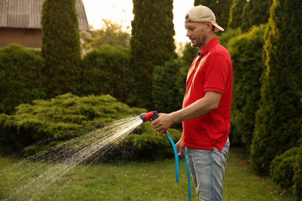 Man deeply watering his lawn to prevent yellow patches and grass discoloration.